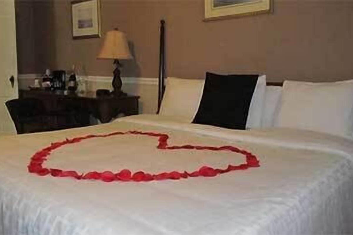 A neatly made bed with a heart-shaped arrangement of rose petals on the bedspread.