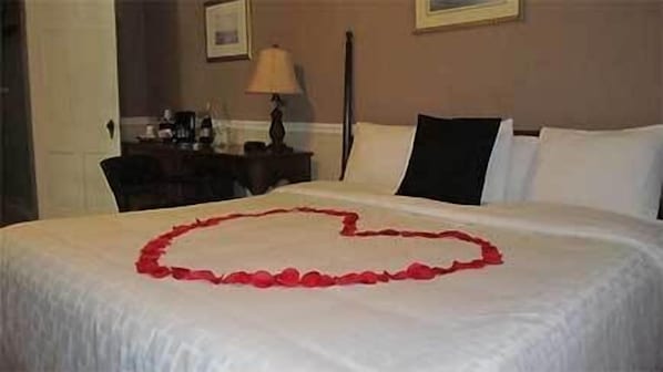 A neatly made bed with a heart-shaped arrangement of rose petals on the bedspread. - Commodore Hotel & Café (Linden)