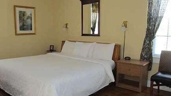 A bedroom with a large bed, a nightstand, a chair, a mirror, and a framed picture on the wall.