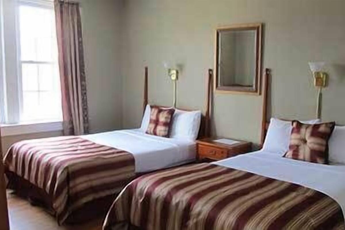 A hotel room with two single beds, a nightstand, a mirror, and a window with curtains.