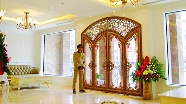 Un vestíbulo de hotel con un amplio separador de madera decorado, candelabros y una planta en maceta con flores.