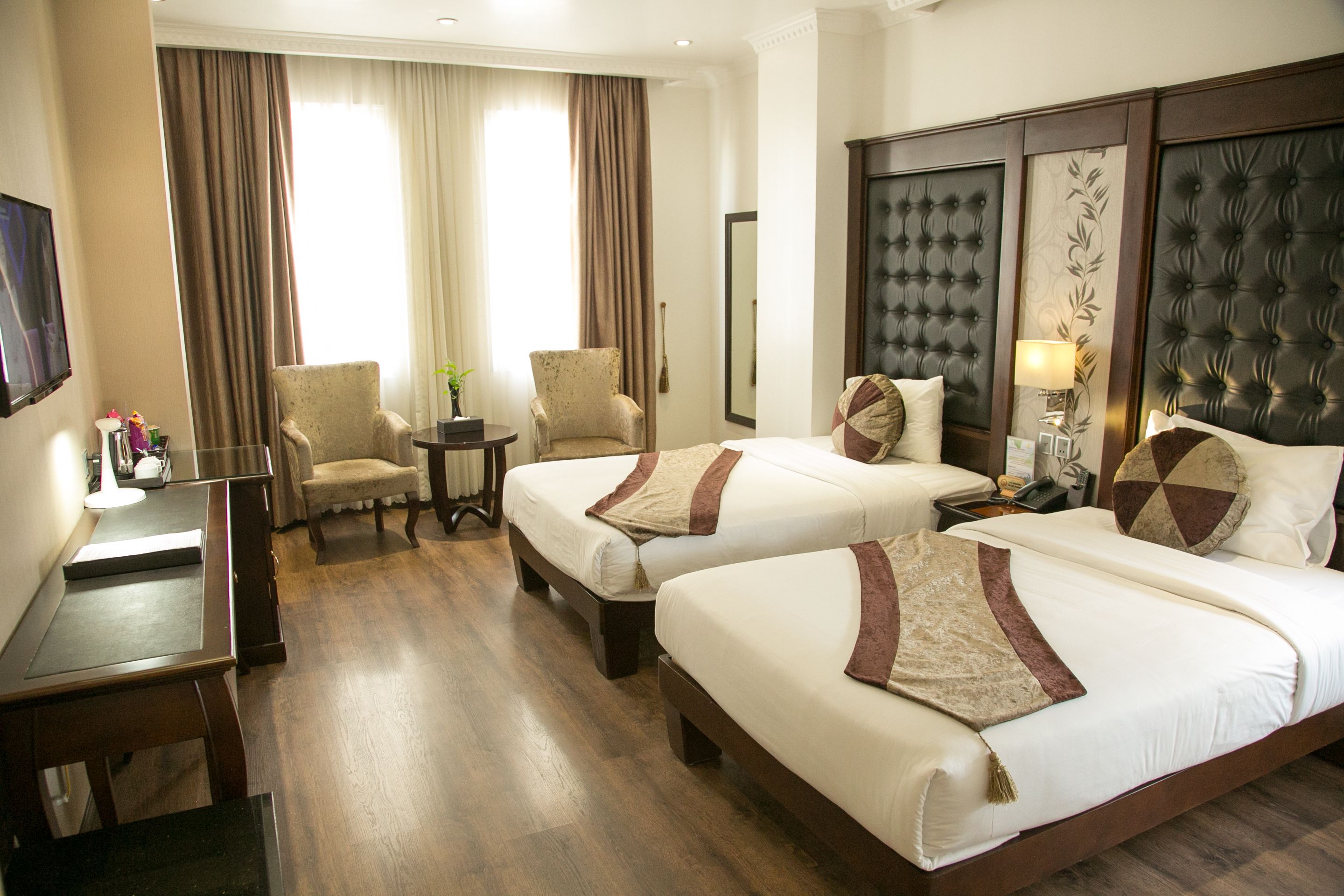 A hotel room with two beds, a desk, a chair, a small table, and a TV.