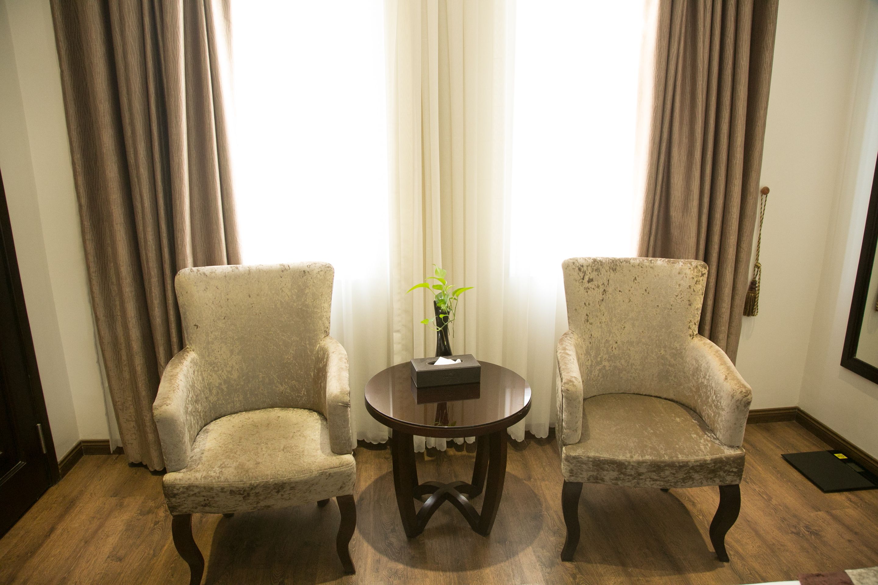 Zwei Sessel, ein kleiner Tisch mit einer Vase und ein Spiegel an der Wand.