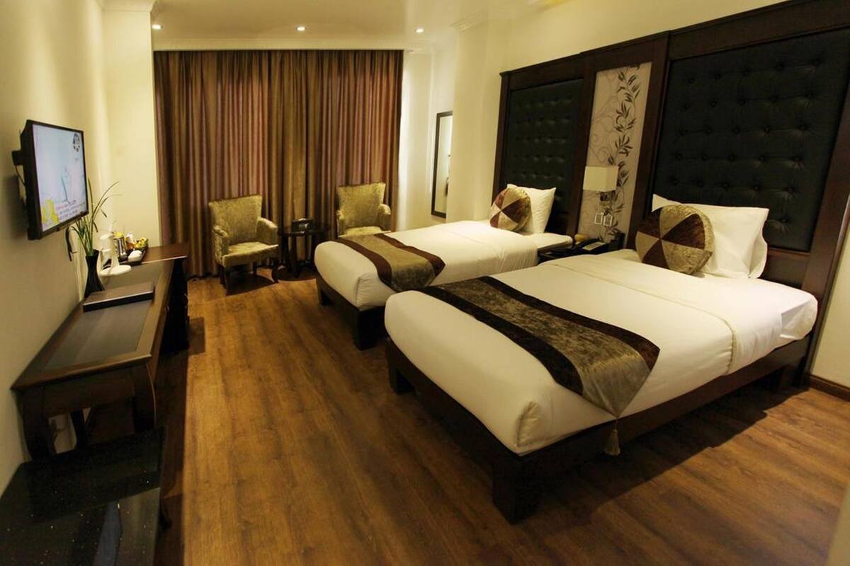 A hotel room with two beds, a desk, a chair, a TV, and a large window with curtains.