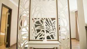 Una habitación con un biombo decorativo con patrones abstractos, piso de madera y una puerta que da a otra estancia.