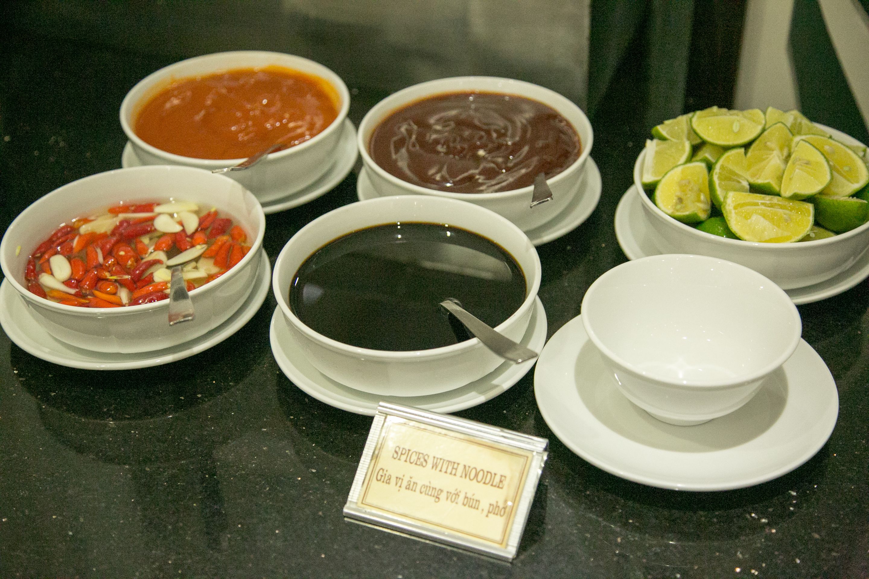 A table with bowls of various soups and a bowl of lime slices.