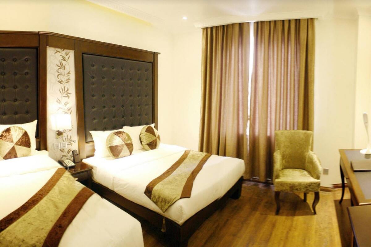 A hotel room with two beds, a chair, a desk, and a TV.