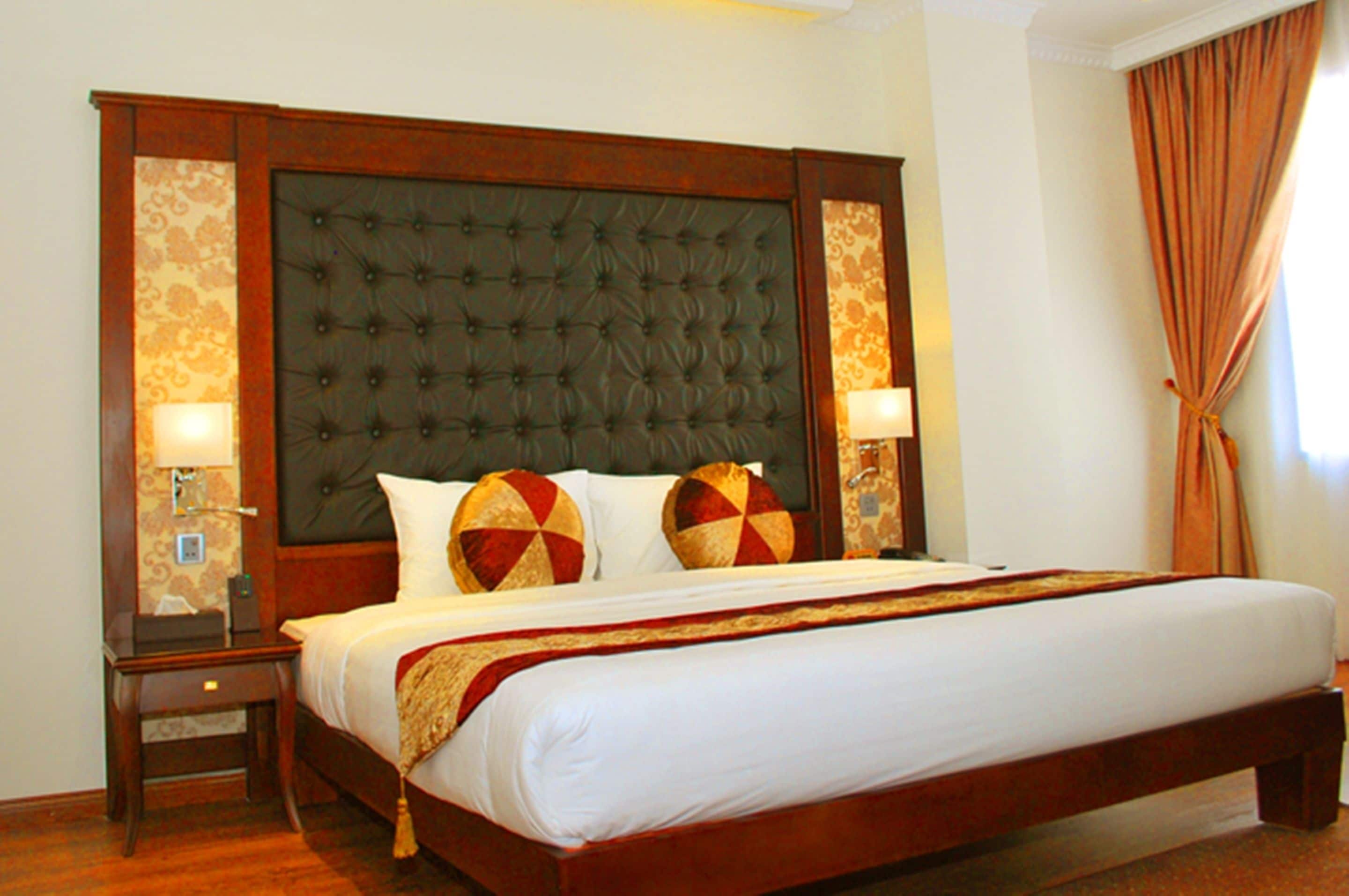 Una cama grande con cabecera capitonada, dos lámparas de noche y almohadas decorativas.