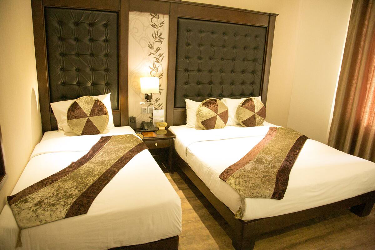 A hotel room with two beds, each with a patterned bedspread and matching pillows. There is a nightstand between the beds with a lamp and a telephone.