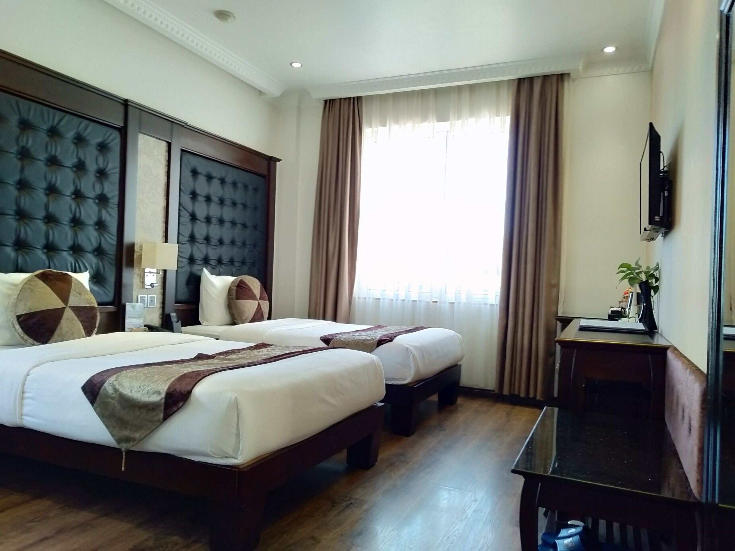 Une chambre d’hôtel avec deux lits, un bureau, une télévision et une grande fenêtre avec des rideaux.