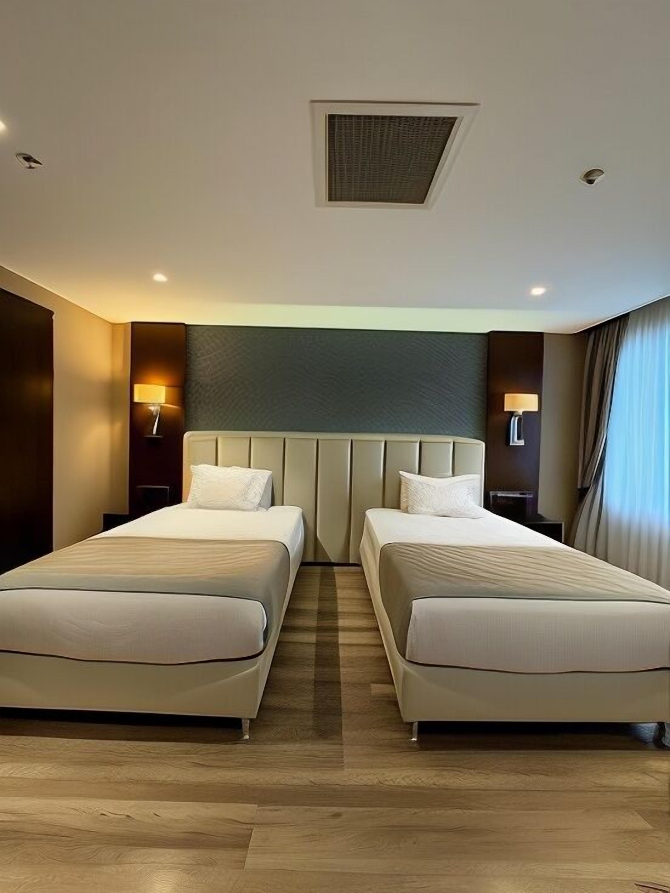 A hotel room with two beds, a ceiling vent, and two bedside lamps.