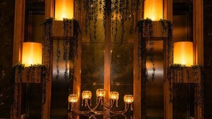 Un candelabro con múltiples luces y plantas colgantes en una habitación con paneles de madera y suelo oscuro.