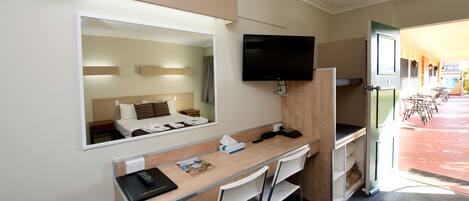 A hotel room with a desk, chairs, a TV, a mirror, and a bed.