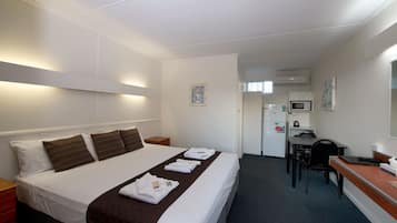A hotel room with a neatly made bed, a desk with a chair, a microwave, and a refrigerator.