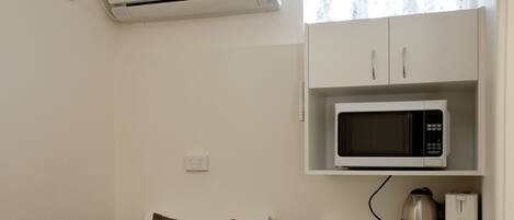 A small, compact room with a bed, a microwave, a refrigerator, and an air conditioning unit.