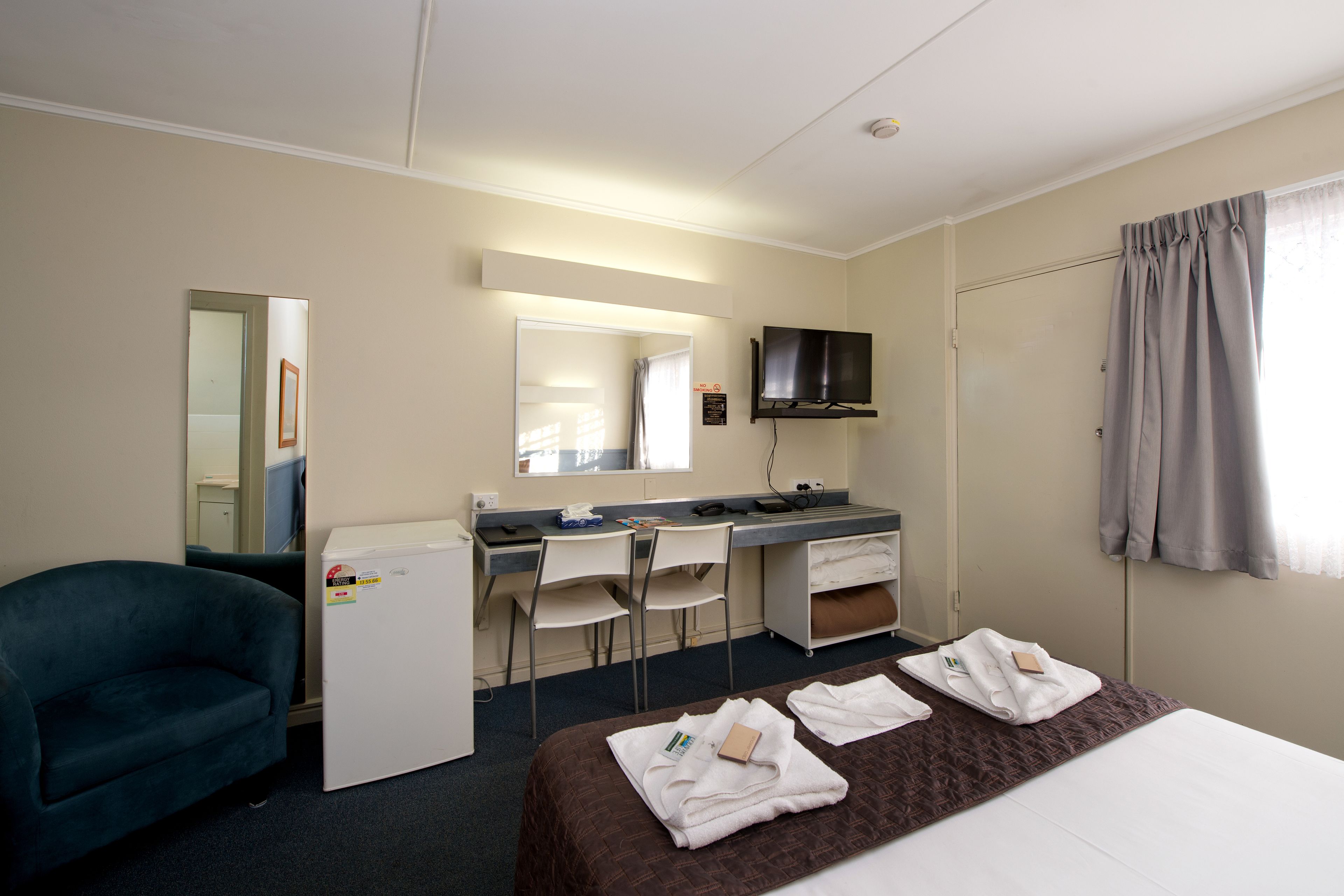 Una habitación de hotel con cama, escritorio, silla, televisor y refrigerador.