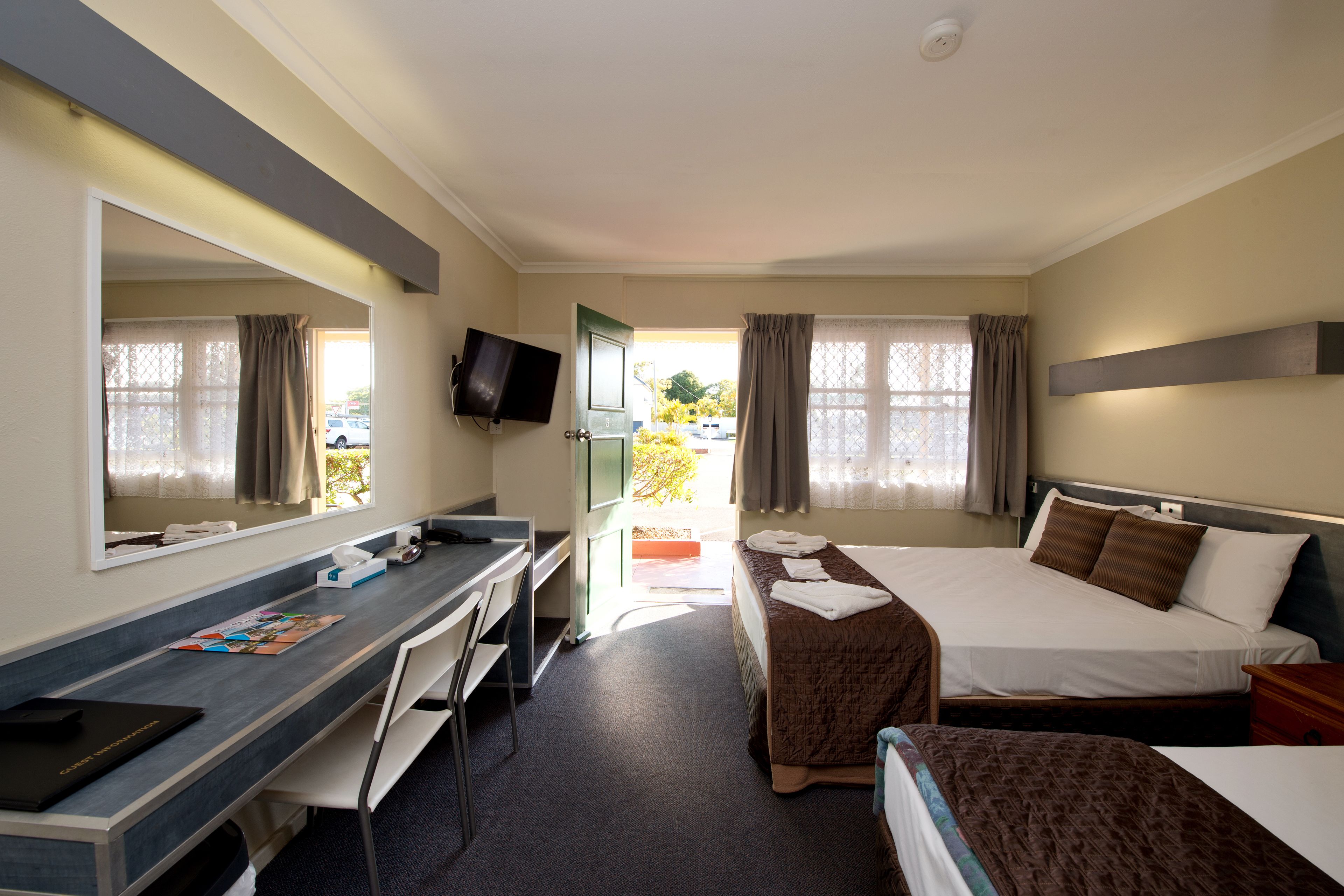 A hotel room with a desk, two beds, a TV, and a window with curtains.