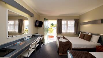 A hotel room with a desk, two beds, a TV, and a window with curtains.