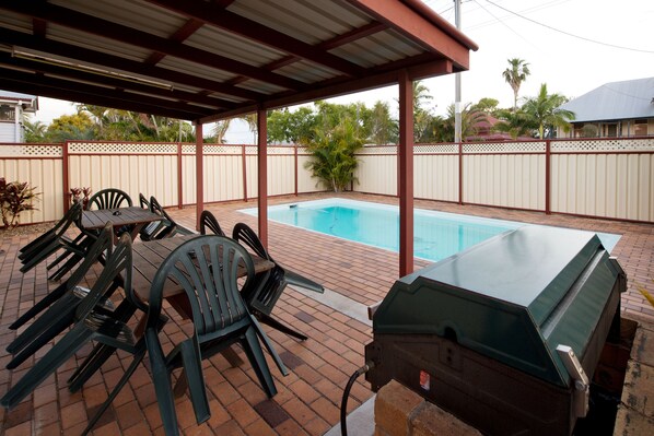 An outdoor patio with a barbecue grill, pool, and seating area.