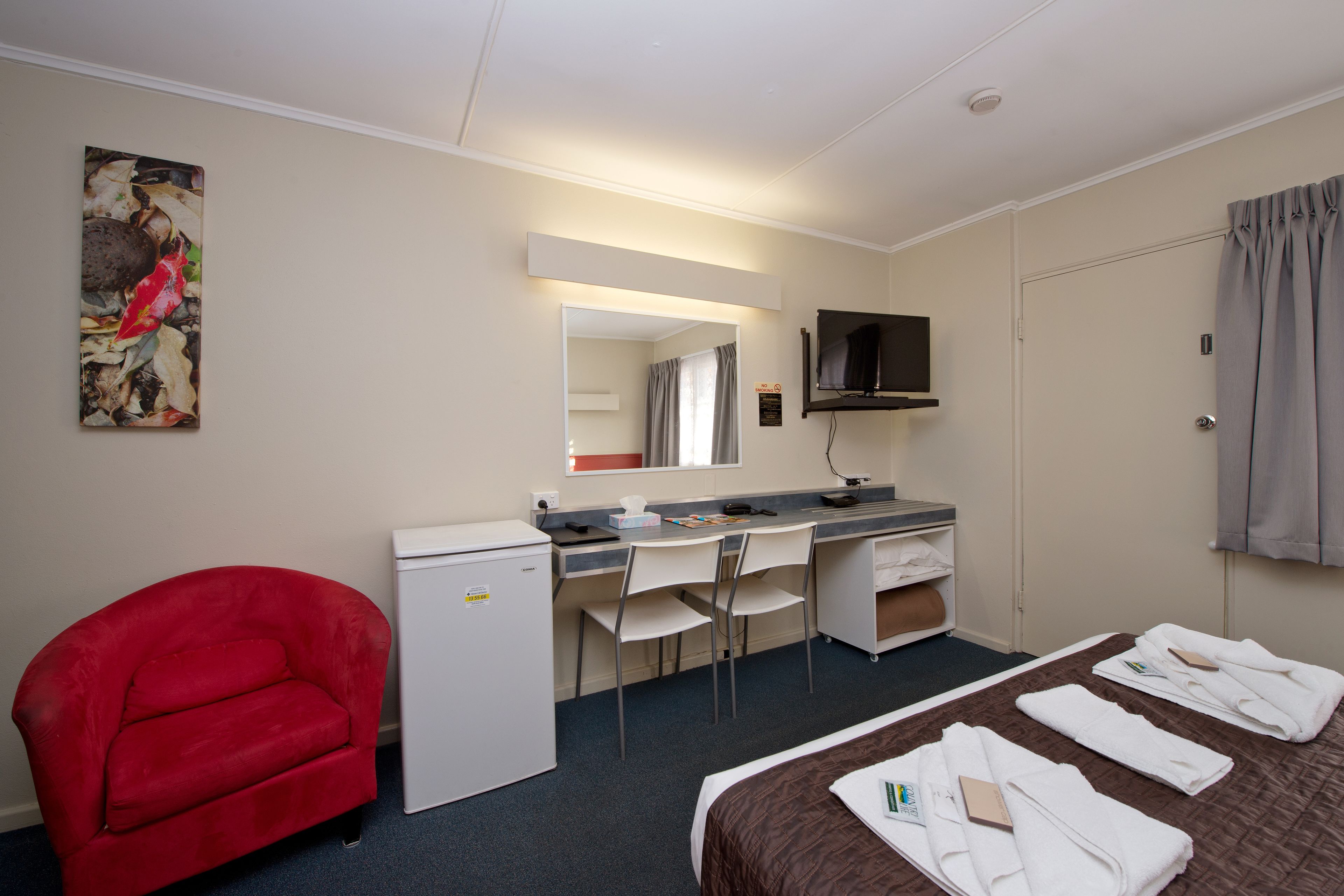 Una habitación de hotel con cama, escritorio, silla, televisor y sillón rojo.