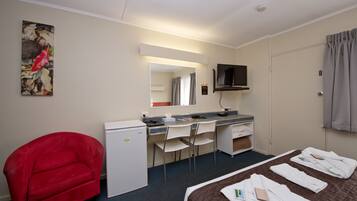 Una habitación de hotel con cama, escritorio, silla, televisor y sillón rojo.