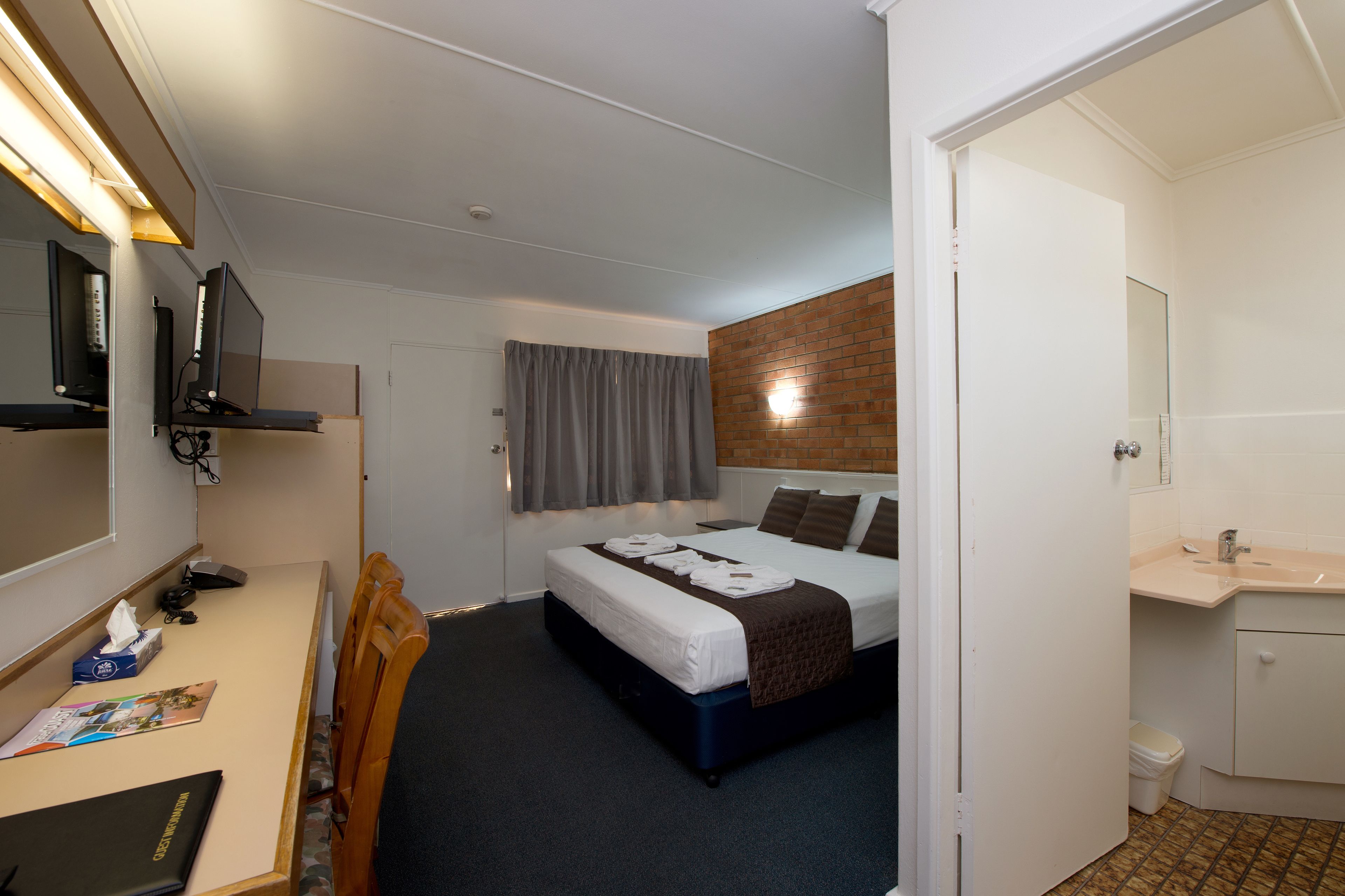 Une chambre d’hôtel comprenant un lit, un bureau avec un ordinateur, une chaise, un miroir et une salle de bain.