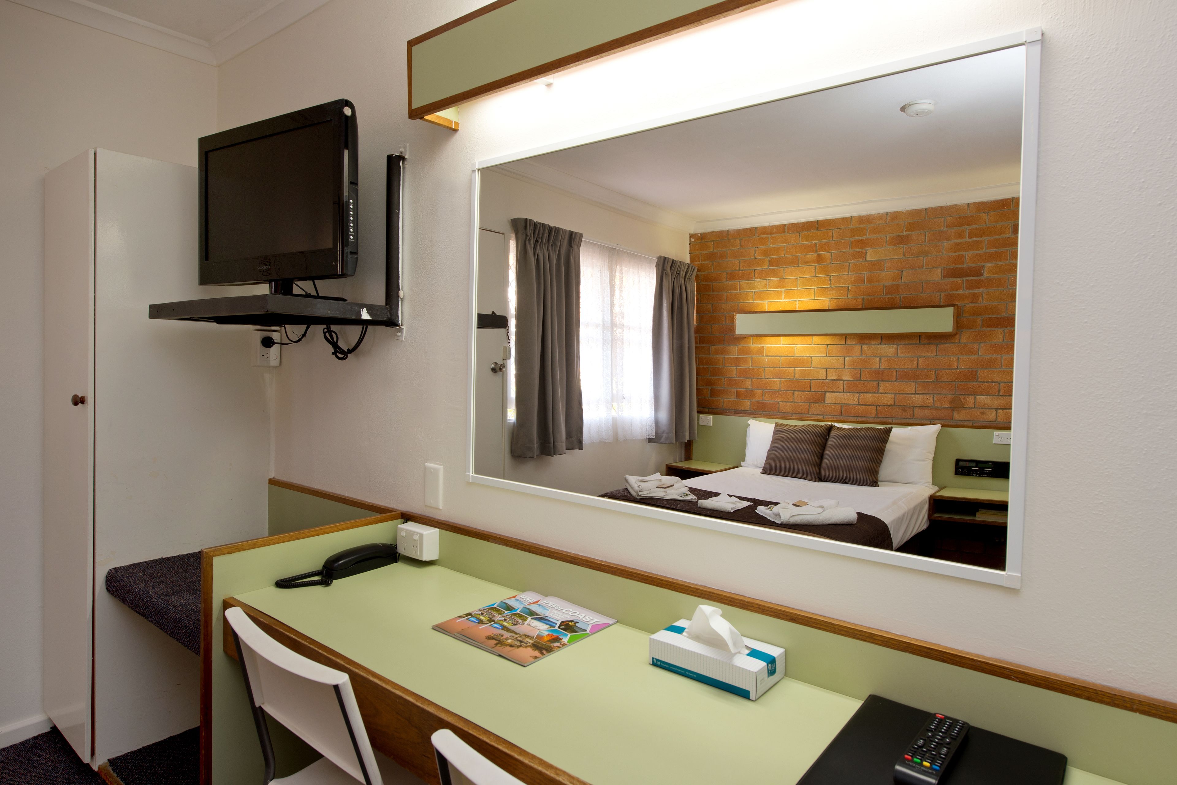 A hotel room with a desk, chair, telephone, and a television mounted on the wall.