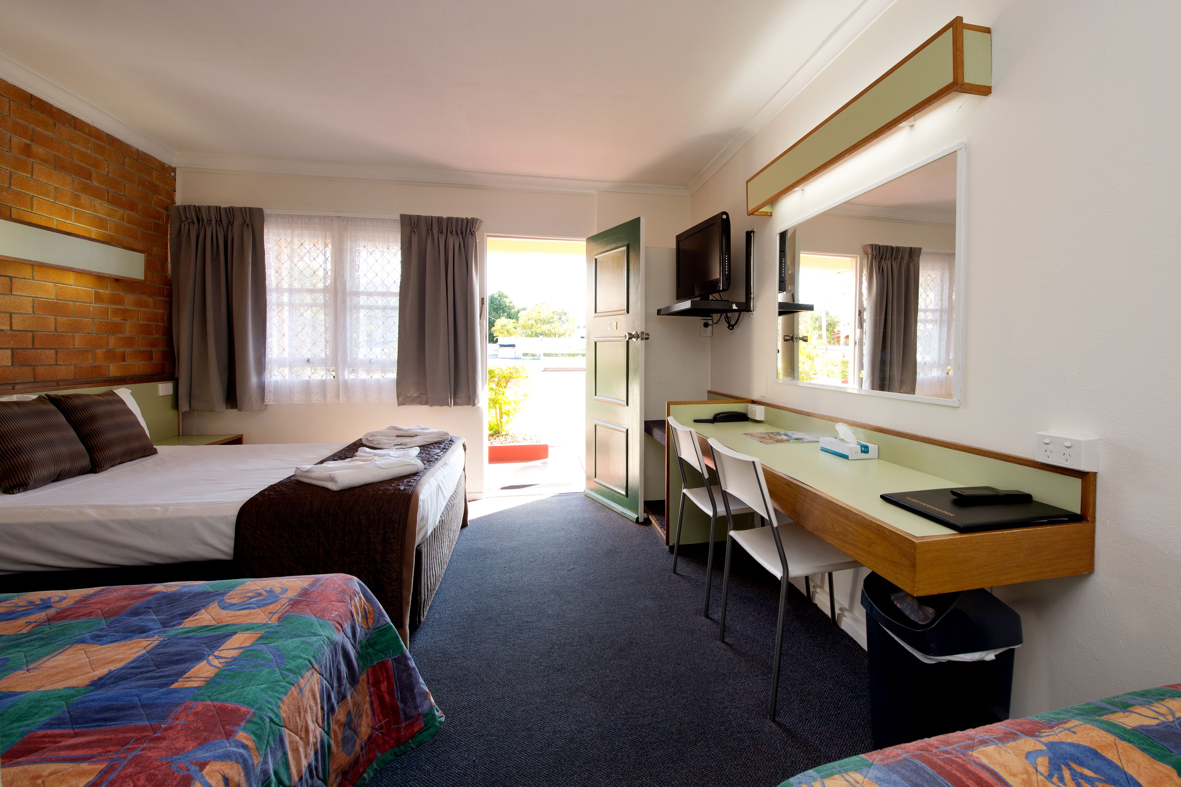 A hotel room with two beds, a desk, a chair, a television, and a window with curtains.