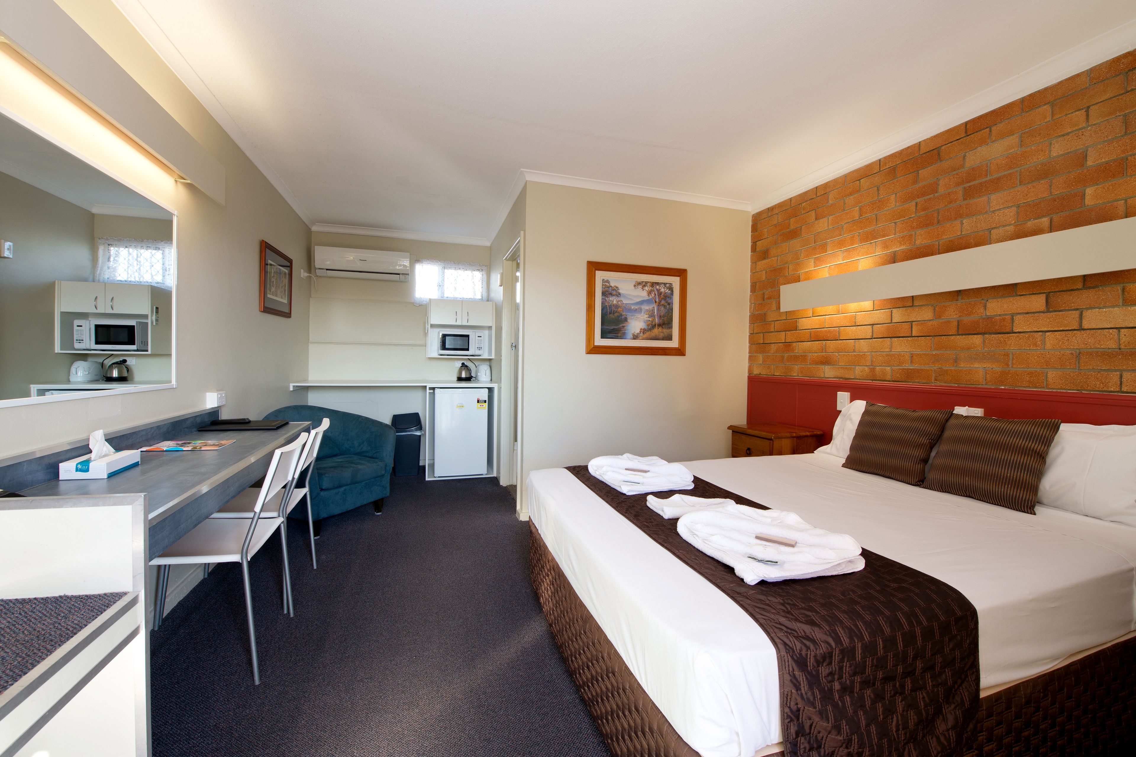 A hotel room with a bed, a desk with a chair, a microwave, and a small kitchenette.