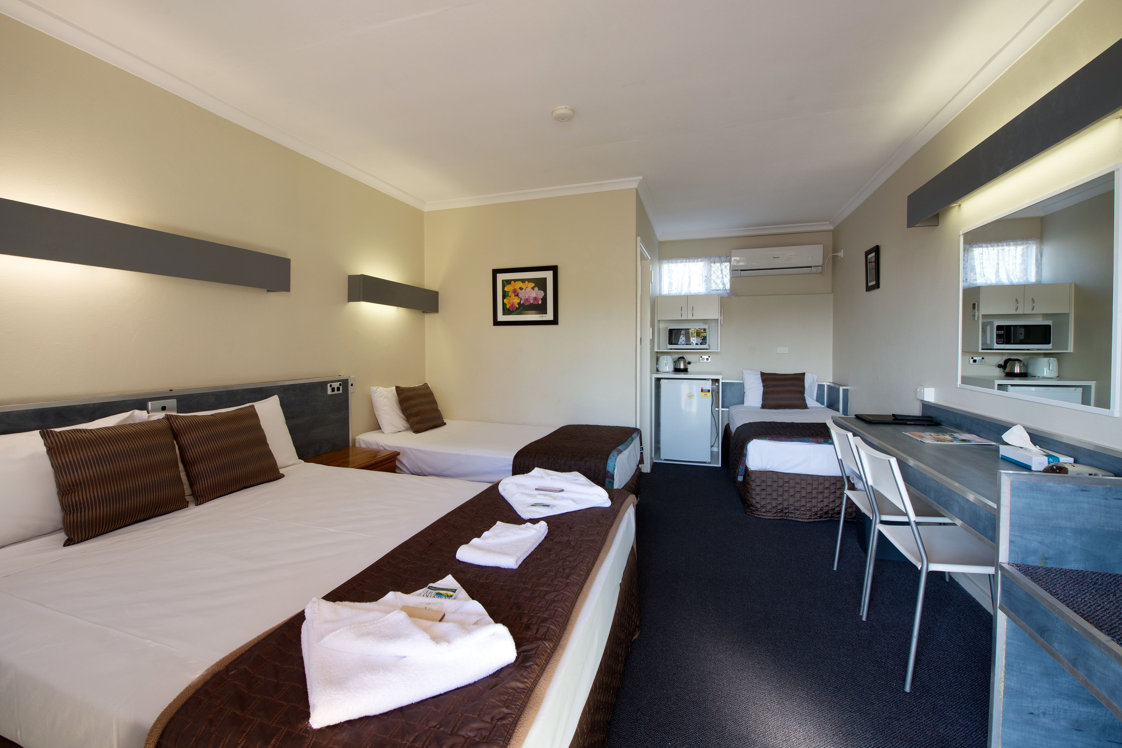A hotel room with two beds, a desk, a chair, a microwave, and a small kitchenette.