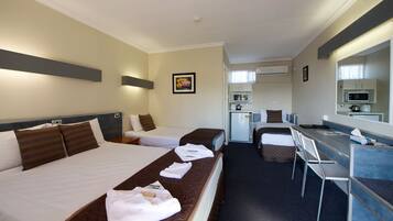 A hotel room with two beds, a desk, a chair, a microwave, and a small kitchenette.