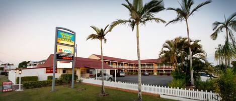 Un motel con un letrero, piscina y estacionamiento cercado.