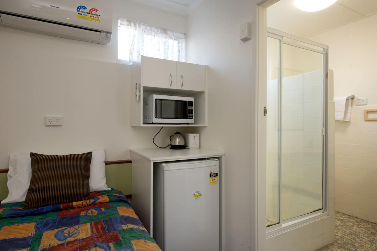 Quarto pequeno e compacto com cama, micro-ondas e frigorífico.