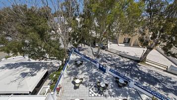 Una terraza en la azotea con asientos al aire libre, árboles y una valla azul.