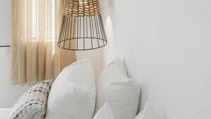 A bedroom with a hanging light fixture, a window with curtains, and two wall-mounted mirrors.