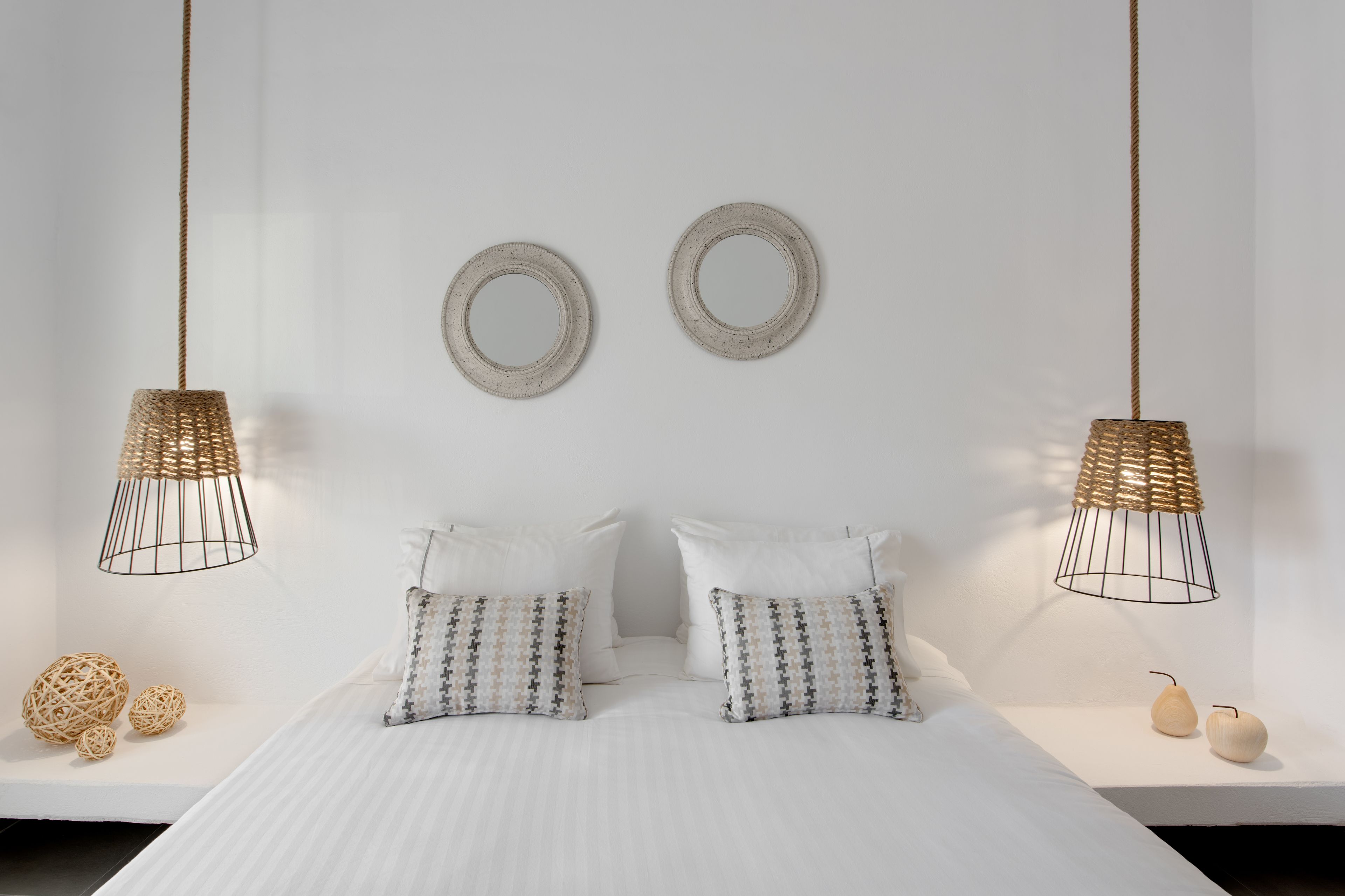 Une chambre à coucher bien rangée, avec un lit, deux lampes suspendues et des coussins décoratifs.