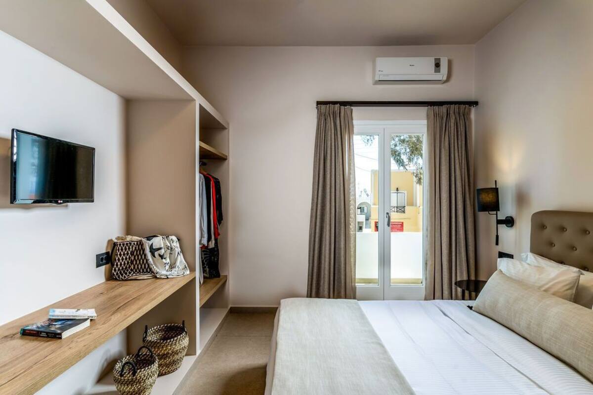 A hotel room with a bed, a TV mounted on the wall, a wardrobe, and a window with curtains.