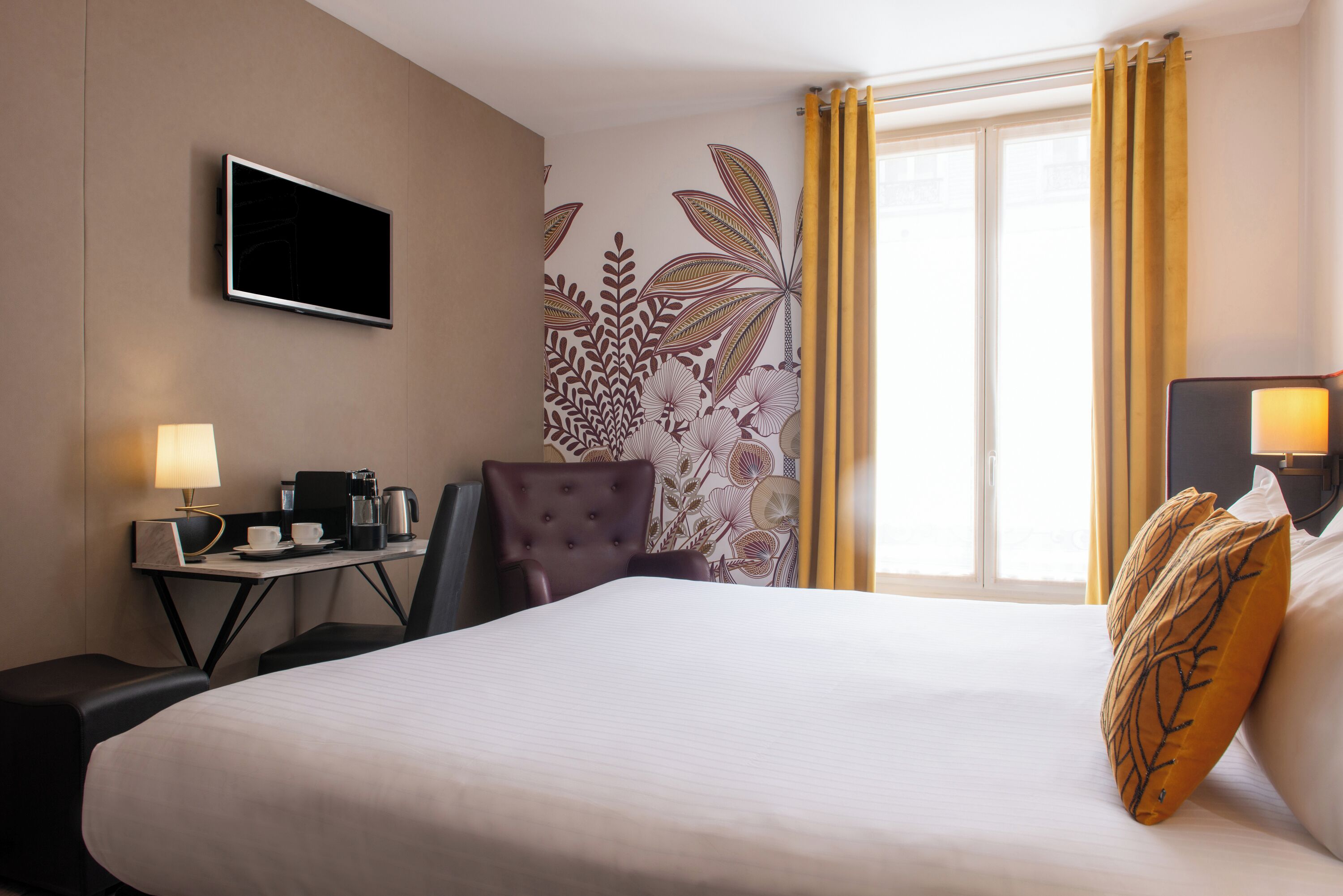 A hotel room with a bed, a desk with a lamp, a chair, and a television on the wall.