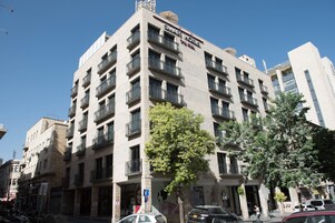 Un hotel de varios pisos con balcones, cielo despejado y coches aparcados.