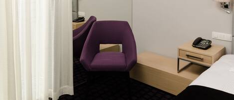 Una habitación de hotel con cama, escritorio, silla, mesita de noche y lámpara.