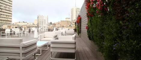 An outdoor seating area with white furniture, a wooden deck, and a wall adorned with flowering plants.