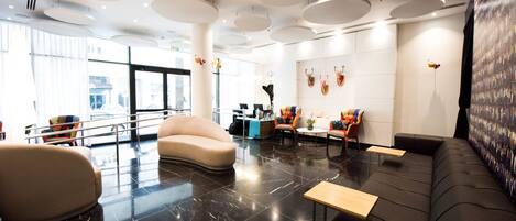 Un lobby moderno con un sofá curvo, una mesa de recepción y una pared con objetos decorativos.