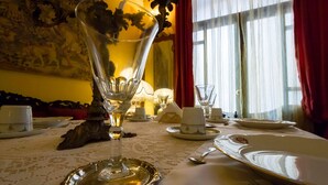 Une table à manger dressée avec de la belle porcelaine, de la verrerie et des couverts en argent, agrémentée d’un centre de table décoratif et donnant sur une fenêtre avec des rideaux.