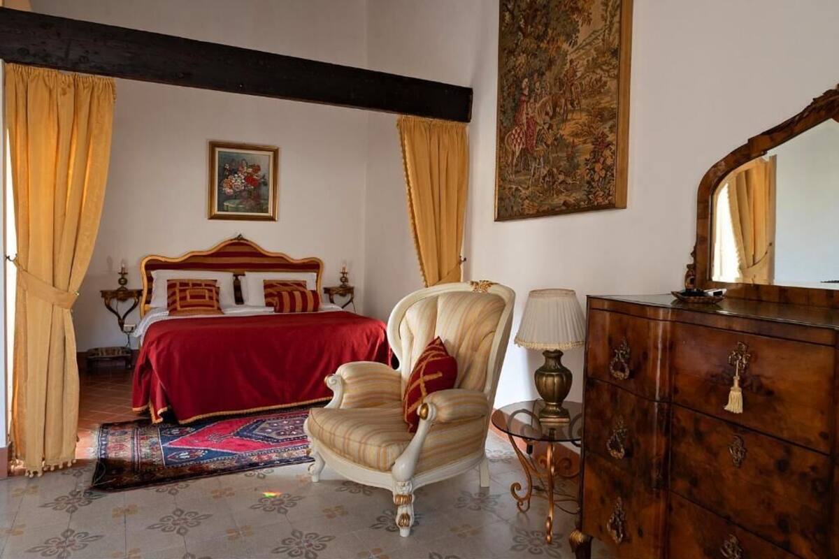 Een slaapkamer met een bed, een stoel, een dressoir en een schilderij aan de muur.