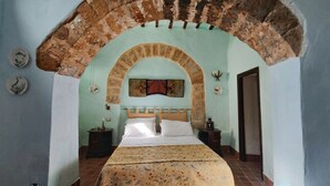 Une chambre à coucher avec un lit placé sous une structure en pierre en forme d’arche, une table de chevet, une lampe et un élément décoratif fixé au mur.