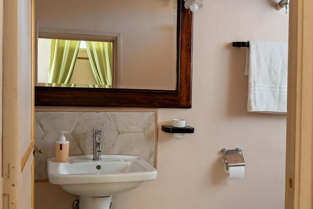 A bathroom with a sink, mirror, towel rack, and toilet paper holder.