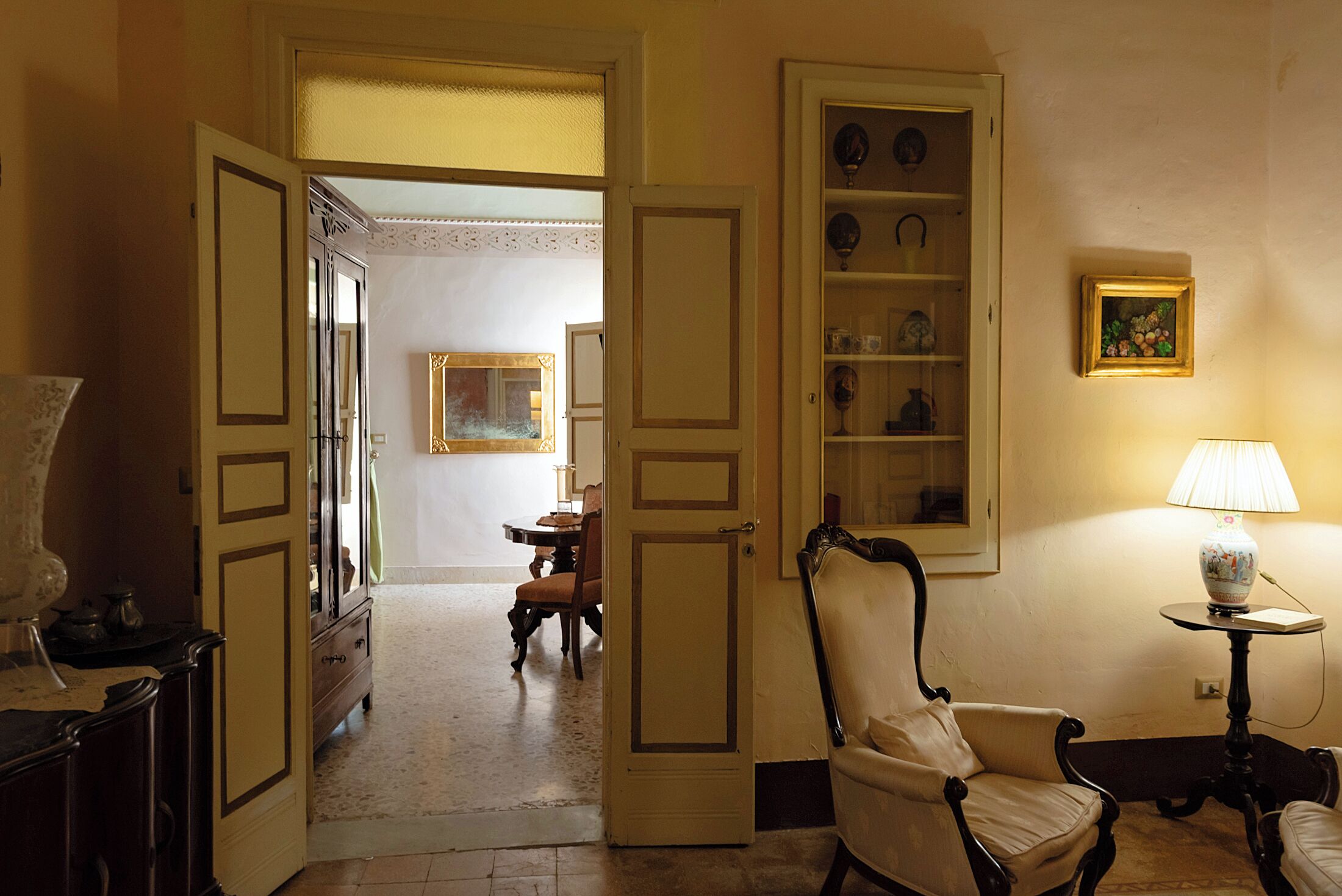 An open doorway leading to a dining area with a table and chairs, a cabinet with glass doors, and a lamp on a side table.