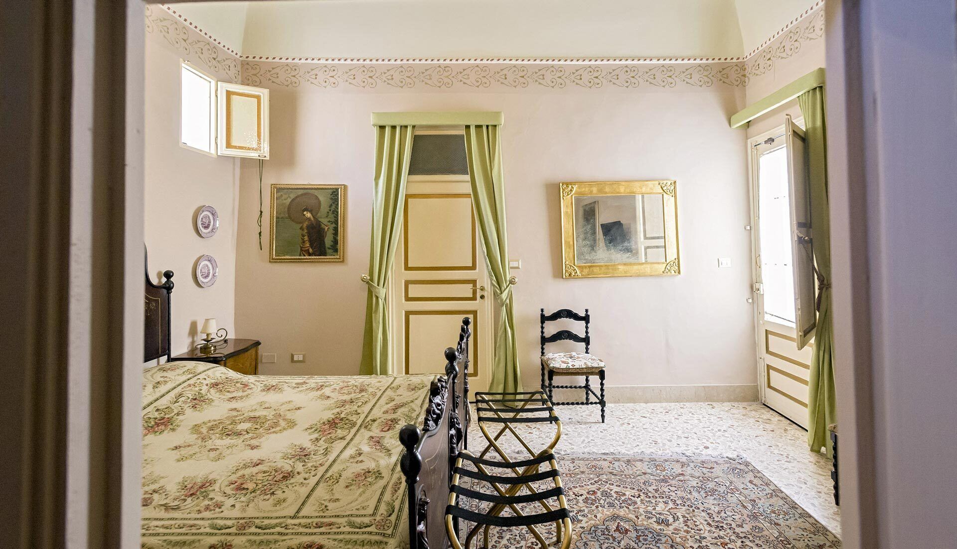 Een slaapkamer met een bed, een stoel, een spiegel en een deur met groene gordijnen.