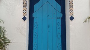 Une porte bleue surmontée d’un toit en forme de triangle, encadrée de carreaux décoratifs, le tout intégré dans un mur blanc.