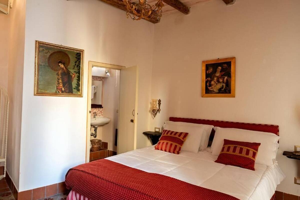 Een slaapkamer met een bed, een spiegel, een kroonluchter en twee schilderijen aan de muur.